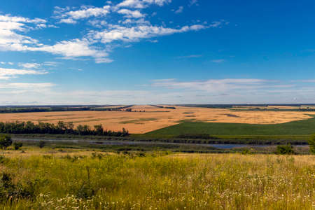 Summer, landscape with a view of the meadow, fields, river and blue sky. Sunny summer scene with river, fields, green hills and beautiful clouds in the blue sky. nice panoramic view.の写真素材