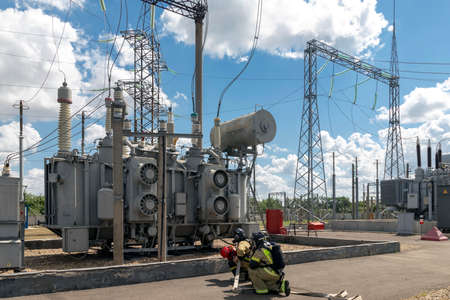 Professional firefighters, rescuers in protective firefighting suits, helmets and gas masks are ready to save people from danger with a fire hose, water hose at an electrical substation.の写真素材