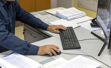 Close-up of a specialist working at a computer in the monitoring and control room. He types on the keyboard and moves the mouse. selective focus.の写真素材