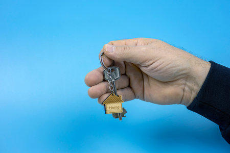 close-up of a hand with house keys and a keychain in the form of a wooden house. The concept of buying a house, rent, mortgage.の写真素材