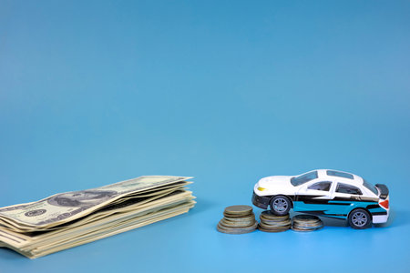 A toy car rides up a stack of coins and dollars.の写真素材
