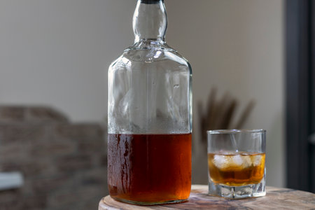 Whiskey glass with ice cubes, misted bottle on wooden tableの写真素材