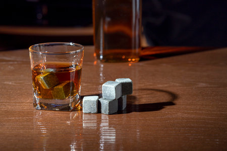 Whiskey in a glass with stones for cooling drinks on a wooden tableの写真素材