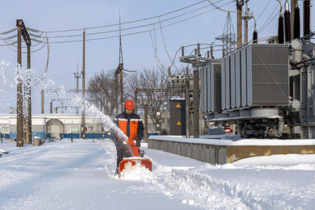 A man with a snowplow is working and removing the snow. On the territory of the electrical substance.の写真素材