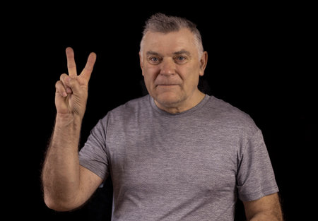Mature man close up portrait, on black background. Close-up of a man with his hand raised against a dark background.の写真素材