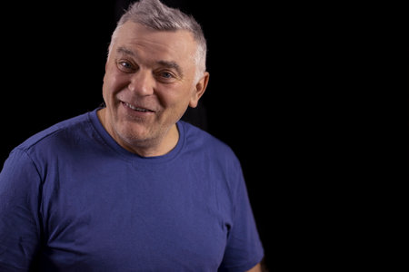 Handsome elderly man with gray hair poses against a black background with copy space and smiles cheerfully.の写真素材