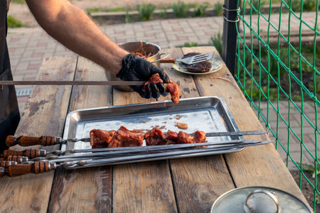 A gloved human hand strings pieces of meat onto a skewer and places them on a metal tray. outdoor video.の写真素材