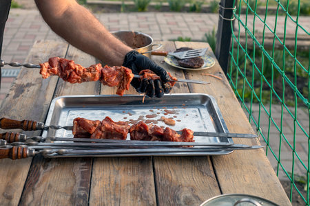 Cook with sterile gloves, pieces of meat on barbecue skewers. Close-up of male hands dressing raw pieces on a metal blade for preparing a dish on a barbecue.の写真素材