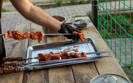 The chef's hands in gloves thread the meat on a barbecue skewer. close-up of raw meat on skewer and street food festivalの写真素材