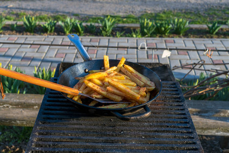 hot food. delicious potatoes are fried in a large frying pan in oil outside. fried potatoes in nature.の写真素材