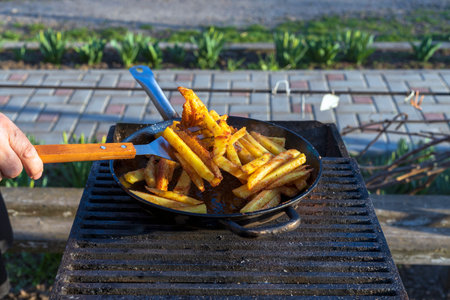hot food. delicious potatoes are fried in a large frying pan in oil outside. fried potatoes in nature.の写真素材