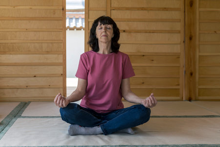 Full length photo of a woman sitting on a mat doing yoga in a meditation room in a Japanese garden.の写真素材