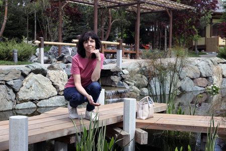 Photo of a mature woman, in the park alone breathing fresh air and admiring the flowers.の写真素材