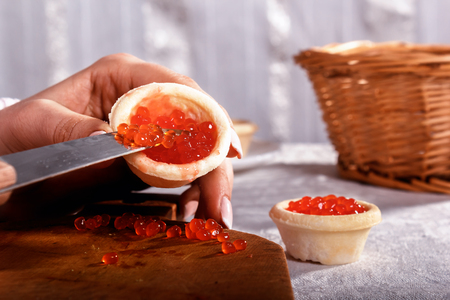 Woman's hands fill a tartlet with red caviar by means of a knifeの写真素材