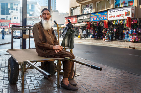 Dubai, UAE - January 9, 2017. Street porter with a cart waiting for work. Unidentified person an elderly man with a gray beard sits on a freight trolley awaiting work in the Deira district, where there are a large number of markets and shops in Dubaiのeditorial素材