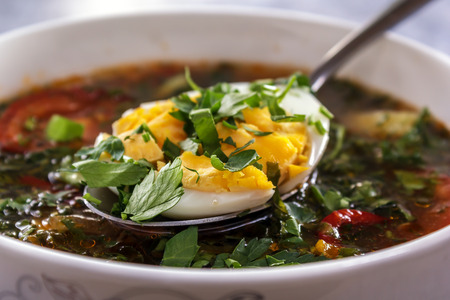Spoon with chopped egg and greens lies on the surface of vegetable soup. Closeupの写真素材