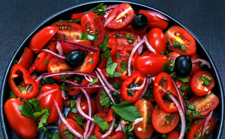 Fresh salad of tomato, onion, pepper, greens and oil on a black plate, black background. Red on blackの写真素材