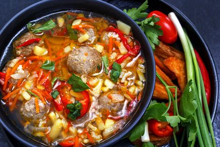 Soup with meatballs in a black plate, sliced ??vegetables - onion, parsley, pepper, tomato on a black backgroundの写真素材