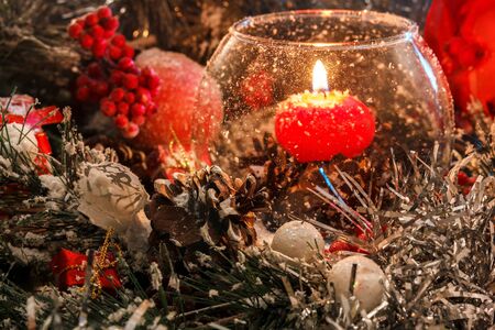 red Christmas candle in a glass on the background of Christmas decorations in the snow. The magic of Christmas and New Yearの写真素材