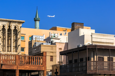 white plane against a blue sky flies over a mosque and colort houses in the oriental style of an old Asian city. District Deira Dubaiの写真素材