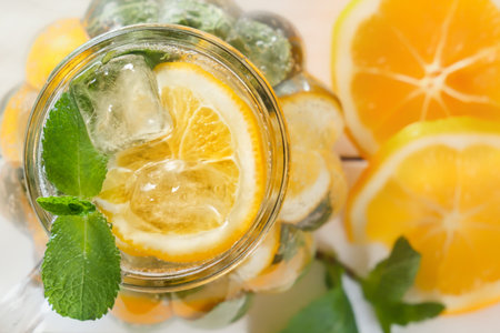 Mason jar of a homemade lemonade with mint and ice, citrus slices on a rustic white wooden...