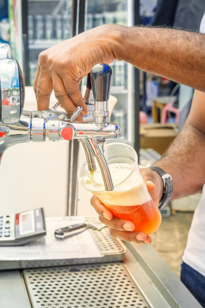 barman's hand holds a large glass in which fresh amber beer is poured with foam. Street tradingの写真素材