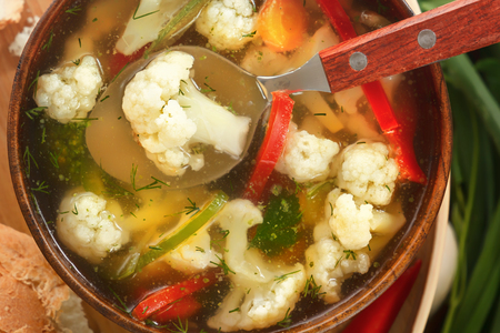 Vegetable soup of cauliflower, carrots, tomato, pepper in a wooden plate with a spoon. Close-upの写真素材