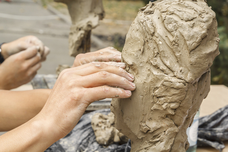 sculptor creates a bust and puts his hands clay on the skeleton of the sculpture. Close-upの写真素材