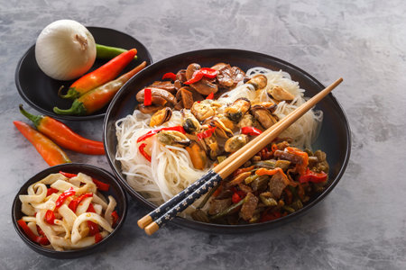 Rice noodles with seafood, salad, fried mushrooms and red pepper stand on a gray table.の写真素材
