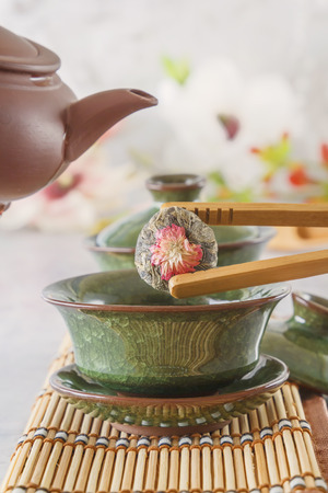bud of green tea is dipped in a traditional Chinese porcelain cup at a tea ceremony with special wooden tweezers.の写真素材