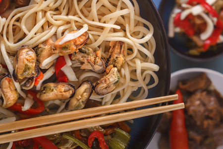 Noodles with seafood, salad, red pepper and fried mushrooms in a porcelain plate. Close-up. Top viewの写真素材