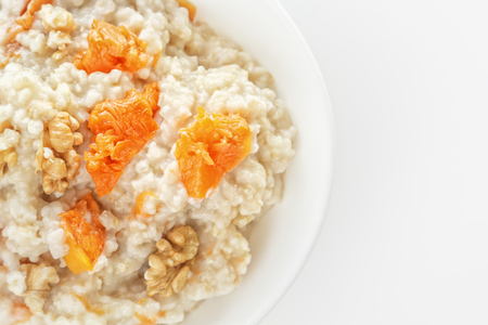 Oatmeal with pumpkin and nuts in a white plate on a white background. View from above. Copy space. Close-upの写真素材