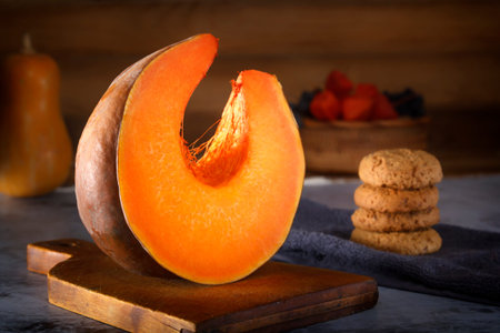 slice of fresh pumpkin on a wooden board against the background of oatmeal cookies and a wicker basket with physalis berries. Close-upの写真素材