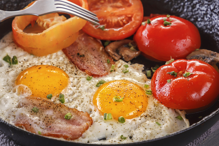 Fried eggs with bacon and tomatoes in an old cast-iron pan. Close-upの写真素材