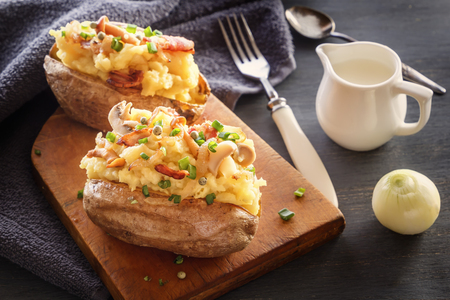 Baked potatoes with bacon and mushrooms in a rustic way on a wooden board. Close-up.の写真素材