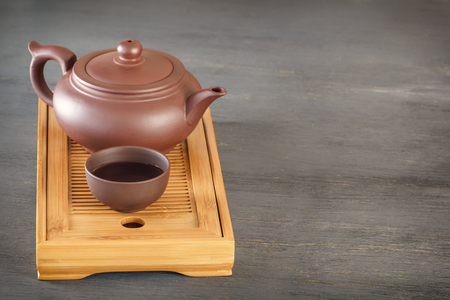 Traditional asian ceramic teapot with a cup stand on a special wooden tea tray on a gray tableの写真素材