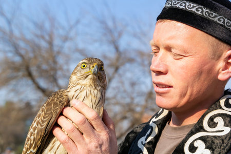 Almaty, Kazakhstan - March 21, 2019. Berkutchi - a hunter with a bird dressed in national clothes, holds a falcon on his hand. Portrait. Close-upのeditorial素材