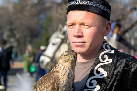 Almaty, Kazakhstan - March 21, 2019. Falcon sits on the hand of a hunter dressed in the national...