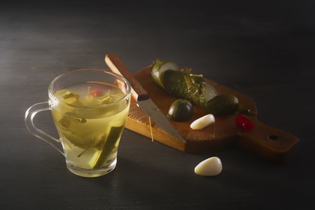Glass with cucumber pickle and pickled cucumbers with a knife on a wooden board. Close-upの写真素材
