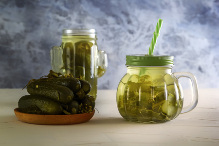 Cucumber pickle in a jar with a lid and tube and pickled cucumbers in a plate on a wooden table. Close-upの写真素材