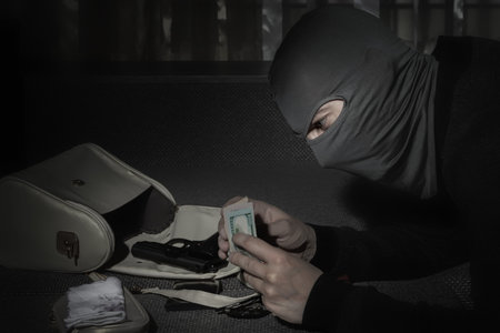 Robber in a mask and with a flashlight examines the contents of the women's bag in a dark room