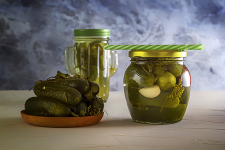 Cucumber pickle in a jar with a lid and tube and pickled cucumbers in a plate on a wooden table. Close-upの写真素材