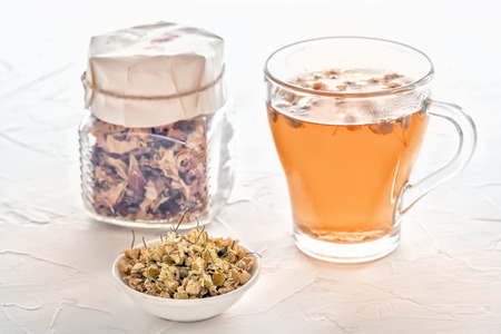 Herbal tea with pharmaceutical chamomile and a jar of dry rose petals on a white table. Close-upの写真素材