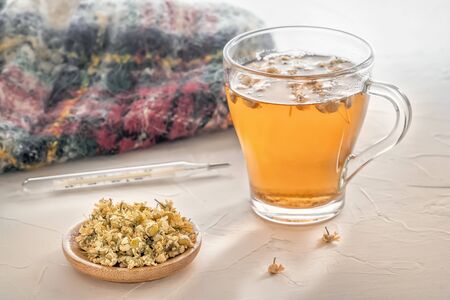 Herbal tea with pharmaceutical chamomile, warm scarf and medical thermometer on a white tableの写真素材