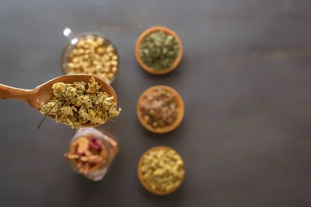 Spoon with pharmaceutical chamomile on the background of medicinal herbs, located on a gray wooden table. View from above. Copy space.の写真素材