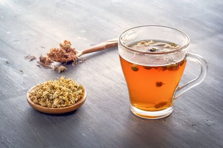 Herbal tea with pharmaceutical chamomile and dry chrysanthemum on a gray wooden tableの写真素材