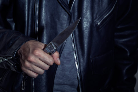 Male hand holding a knife on the background of a leather jacket. Close-up