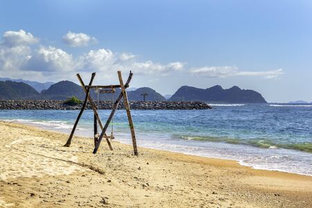 Homemade empty rope swing on a deserted beach against the background of the sea and blue sky with clouds. Copy spaceの写真素材