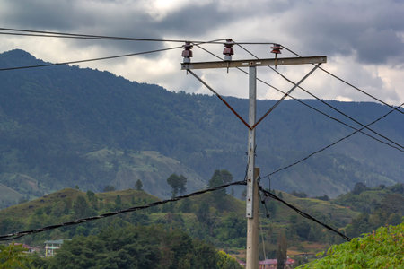 Home-made power pole with wires and old insulators against the backdrop of mountains and sky with...