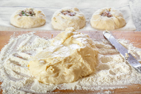 Fresh raw yeast dough on a wooden board with flour on a background of raw pies with meat filling....